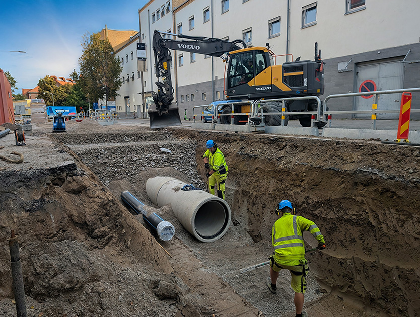 Arbetare gräver ner betongrör i gatan i stadsmiljö